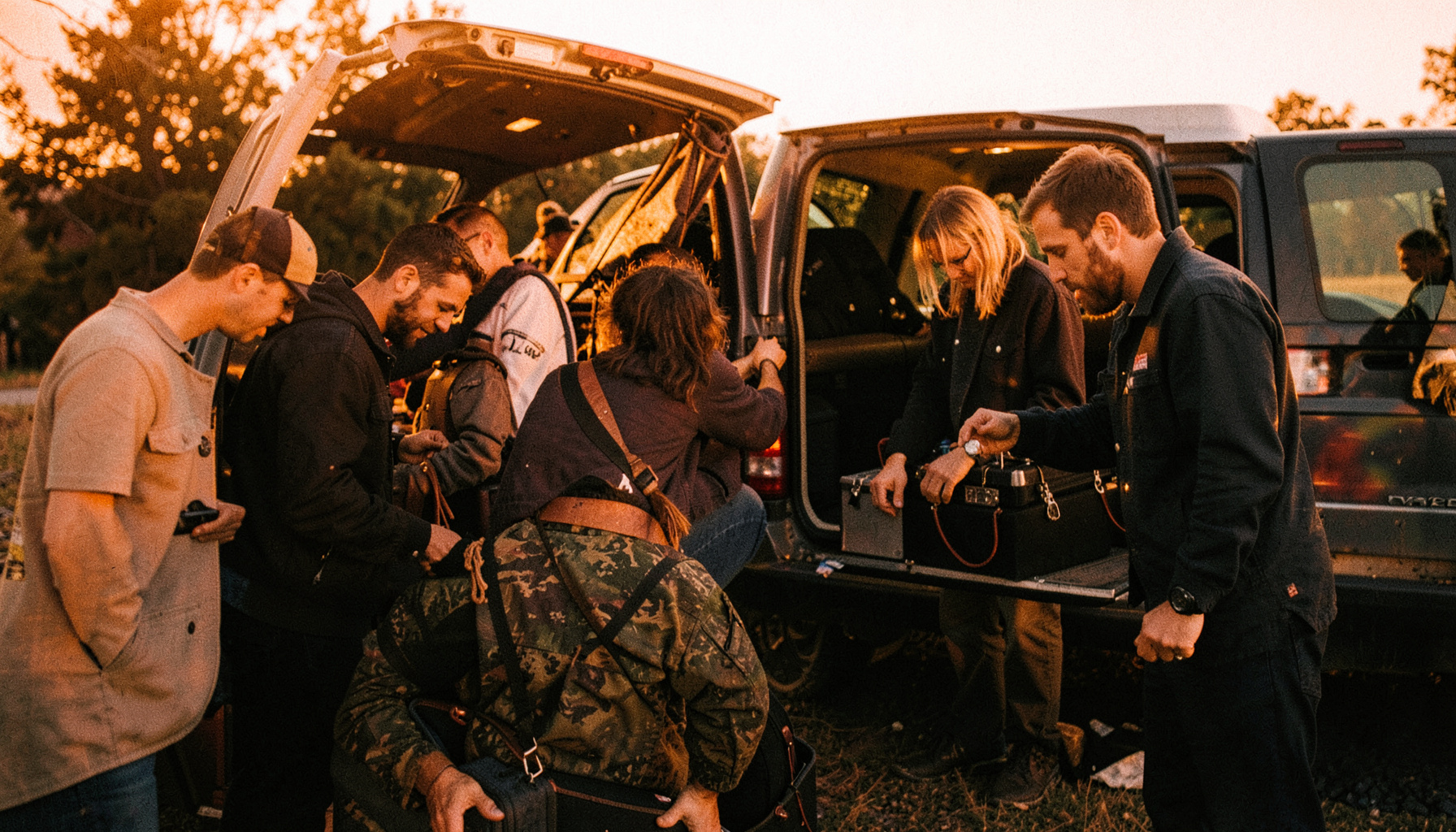 Candid shot of band members loading gear into a van at dusk, golden-hour light