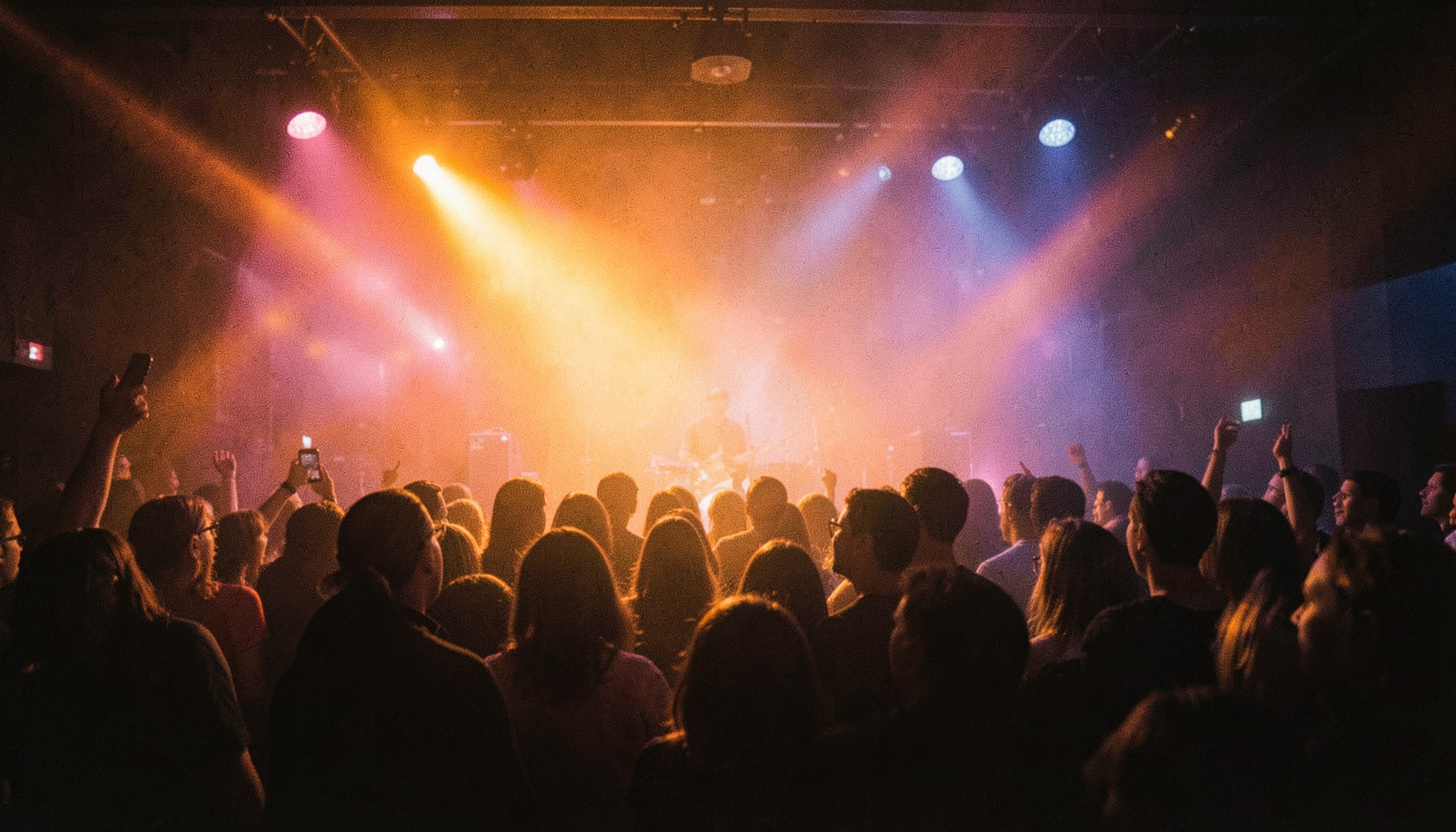 Warm stage lights cutting through haze at a live concert, deep amber and indigo tones, intimate club atmosphere