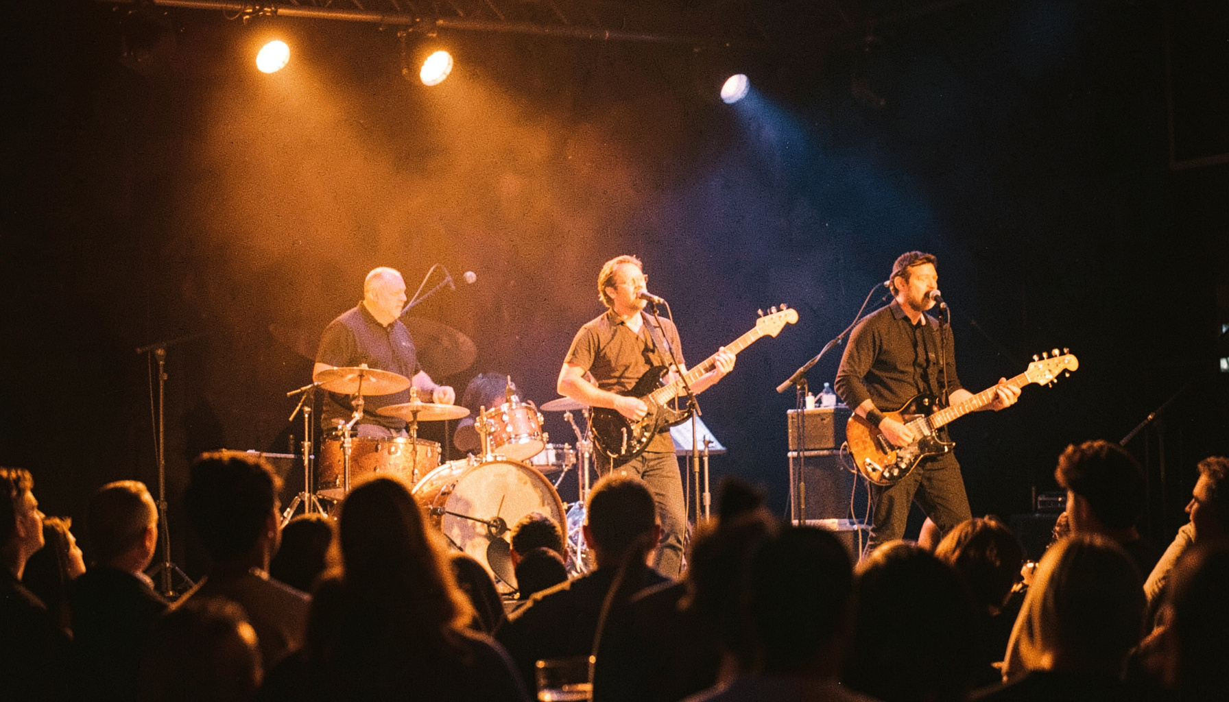 Warm-toned photograph of a live band performing on a dimly lit stage, amber and navy mood